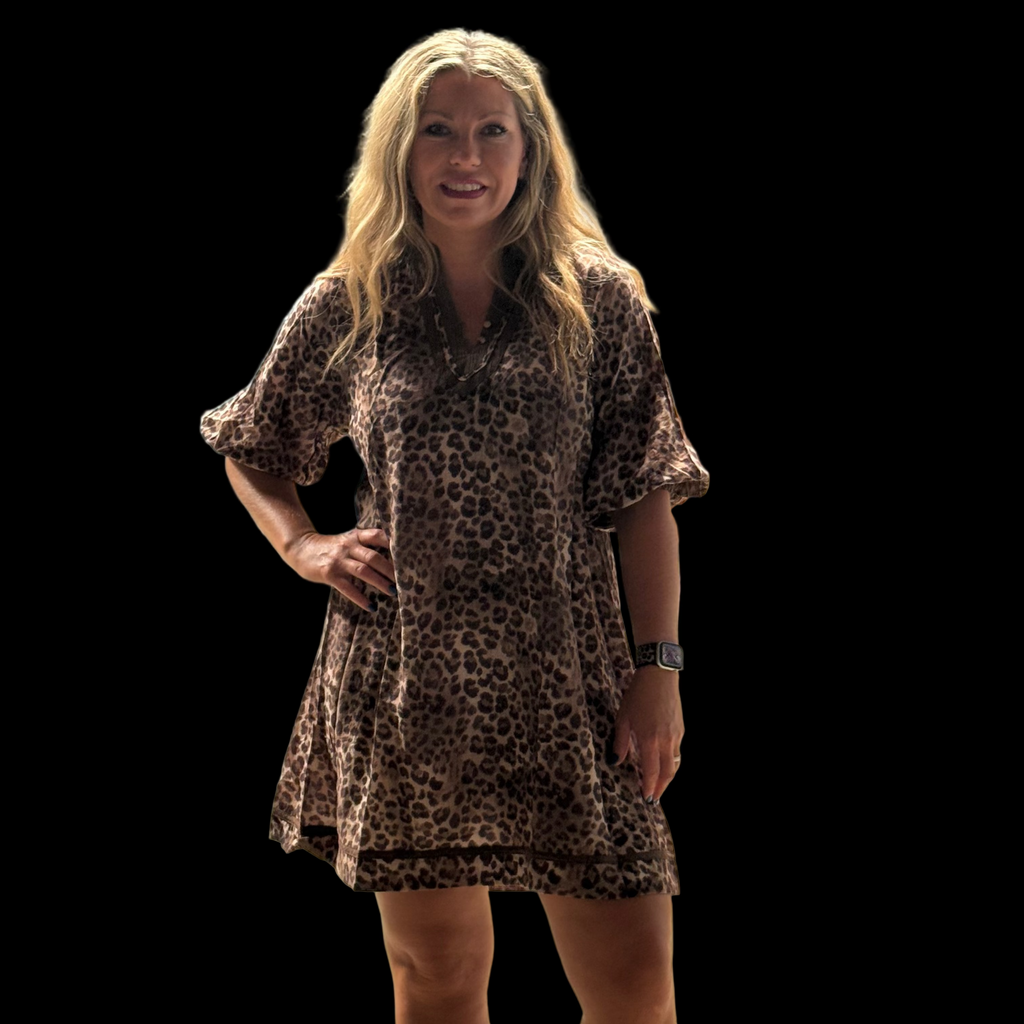 Woman wearing a leopard print dress in an indoor setting with blue curtains and a whiteboard.