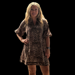 Woman wearing a leopard print dress in an indoor setting with blue curtains and a whiteboard.