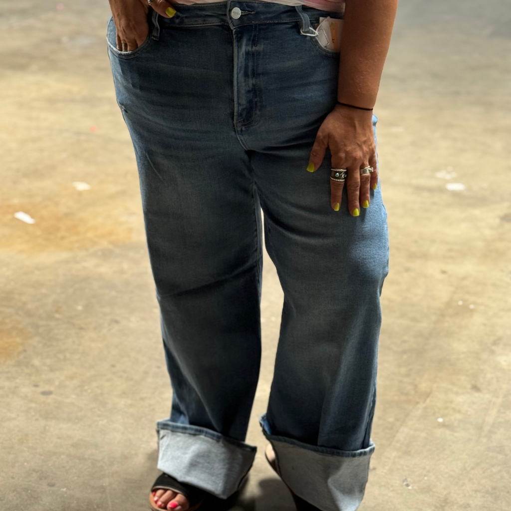 Person wearing blue jeans with rolled-up cuffs on a concrete floor.