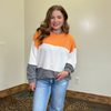 Woman wearing a color-blocked sweater and jeans indoors against a plain wall.