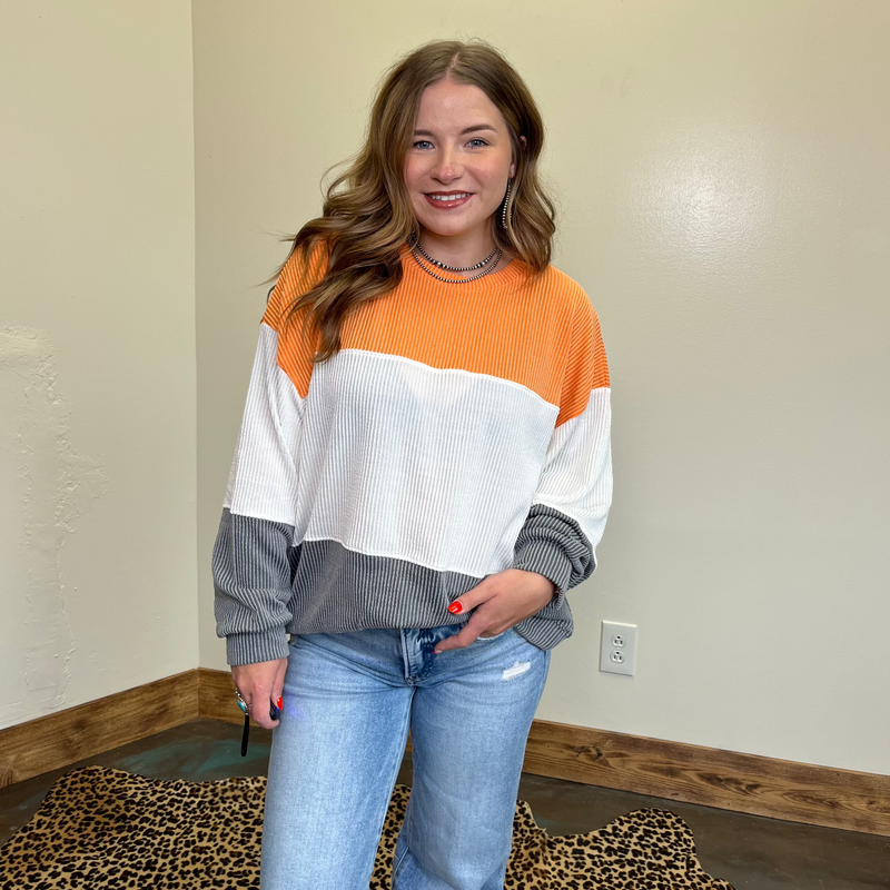 Woman wearing a color-blocked sweater and jeans indoors against a plain wall.