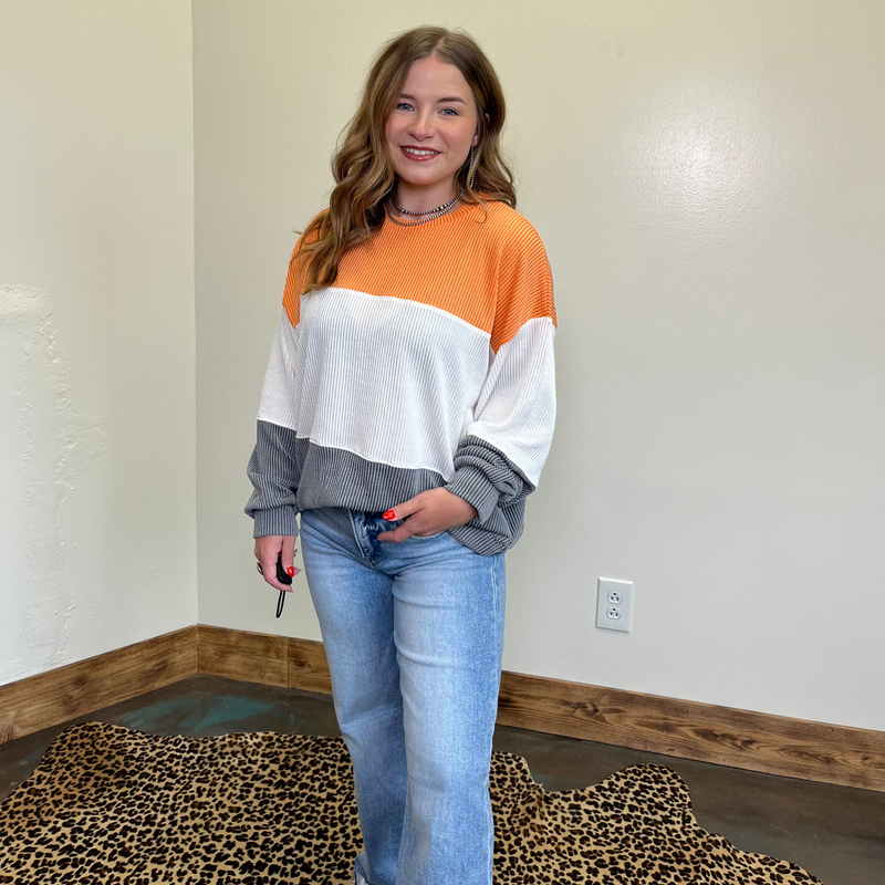 Woman wearing a color-blocked sweater and jeans standing in a room with a plain wall and leopard print rug.