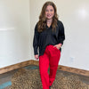 Woman in black top and red pants standing on a leopard print rug in a room with white walls.