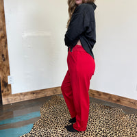 Person wearing red pants and a black jacket standing on a leopard print rug.