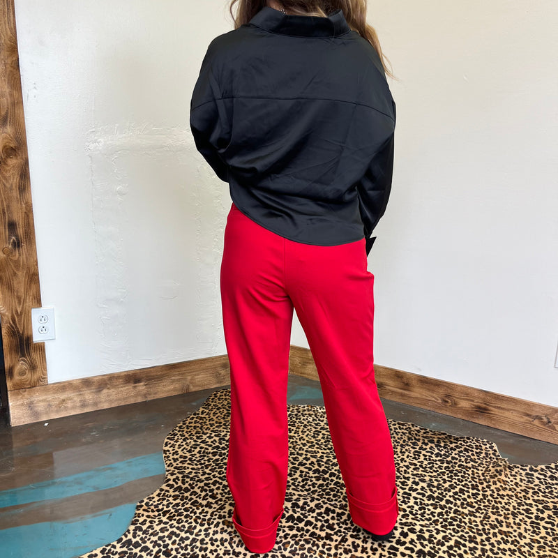 Person wearing a black jacket and red pants standing on a leopard print rug.