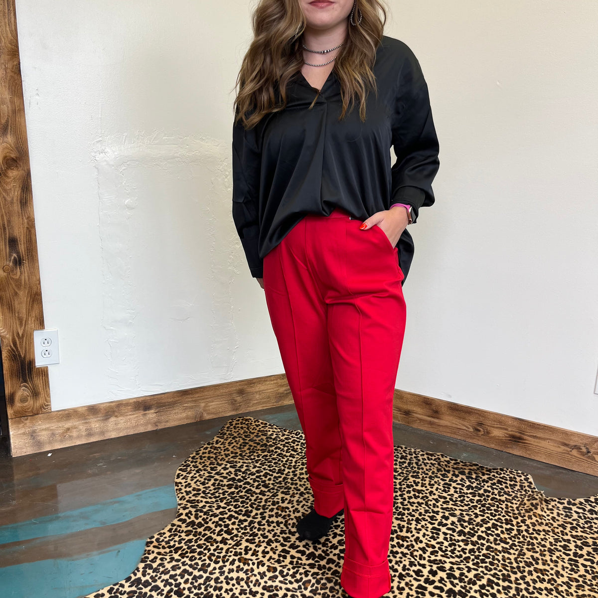 Person wearing a black top and red pants standing on a leopard print rug.