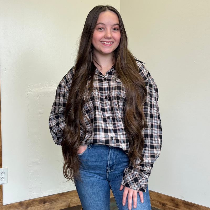 Person wearing a plaid shirt and jeans standing against a wall with wooden trim.