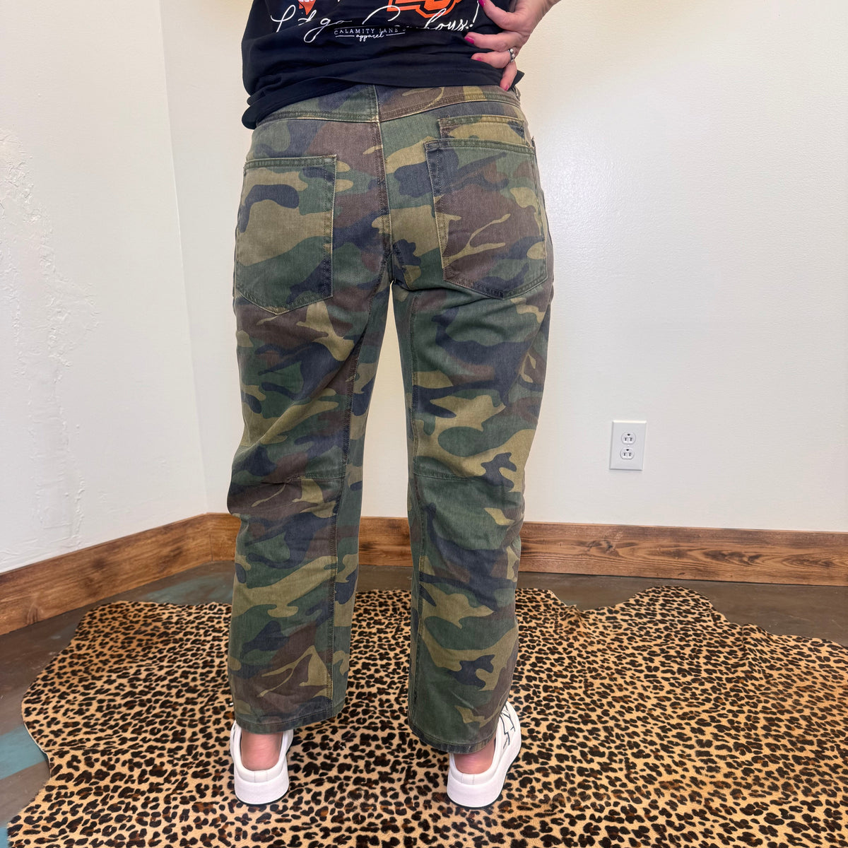 camouflage pants and a black shirt with orange text, standing on a leopard print rug.