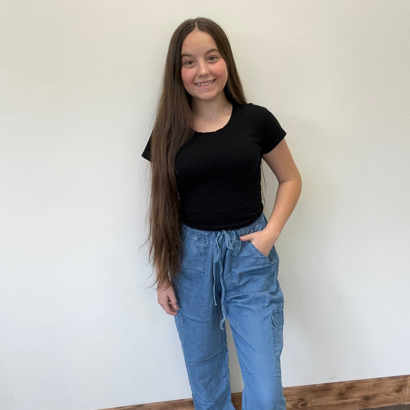 Person wearing a black t-shirt and blue jeans standing against a white wall.
