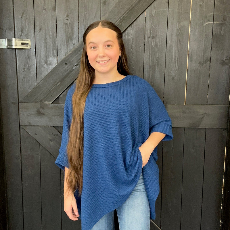 blue sweater and jeans standing against a wooden door.