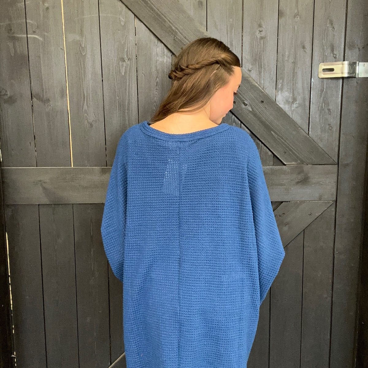 Person wearing a blue sweater standing against a wooden door.