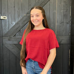 Person wearing a red shirt and blue jeans standing in front of a wooden door.
