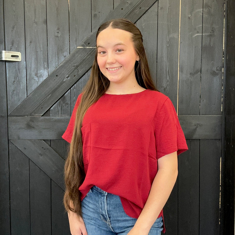 Person wearing a red shirt and blue jeans standing in front of a wooden door.