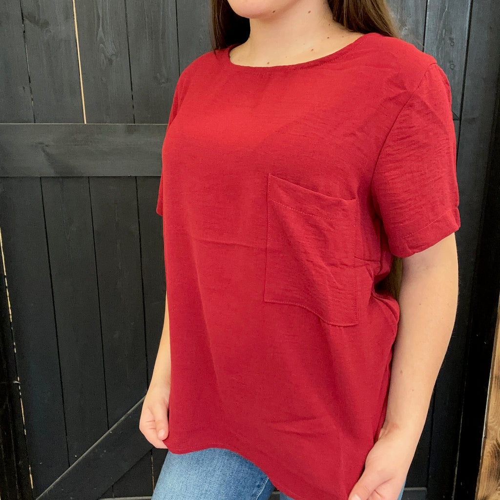 Person wearing a red t-shirt with a pocket against a dark wooden background
