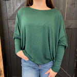 Person wearing a green long-sleeve top and blue jeans against a wooden background