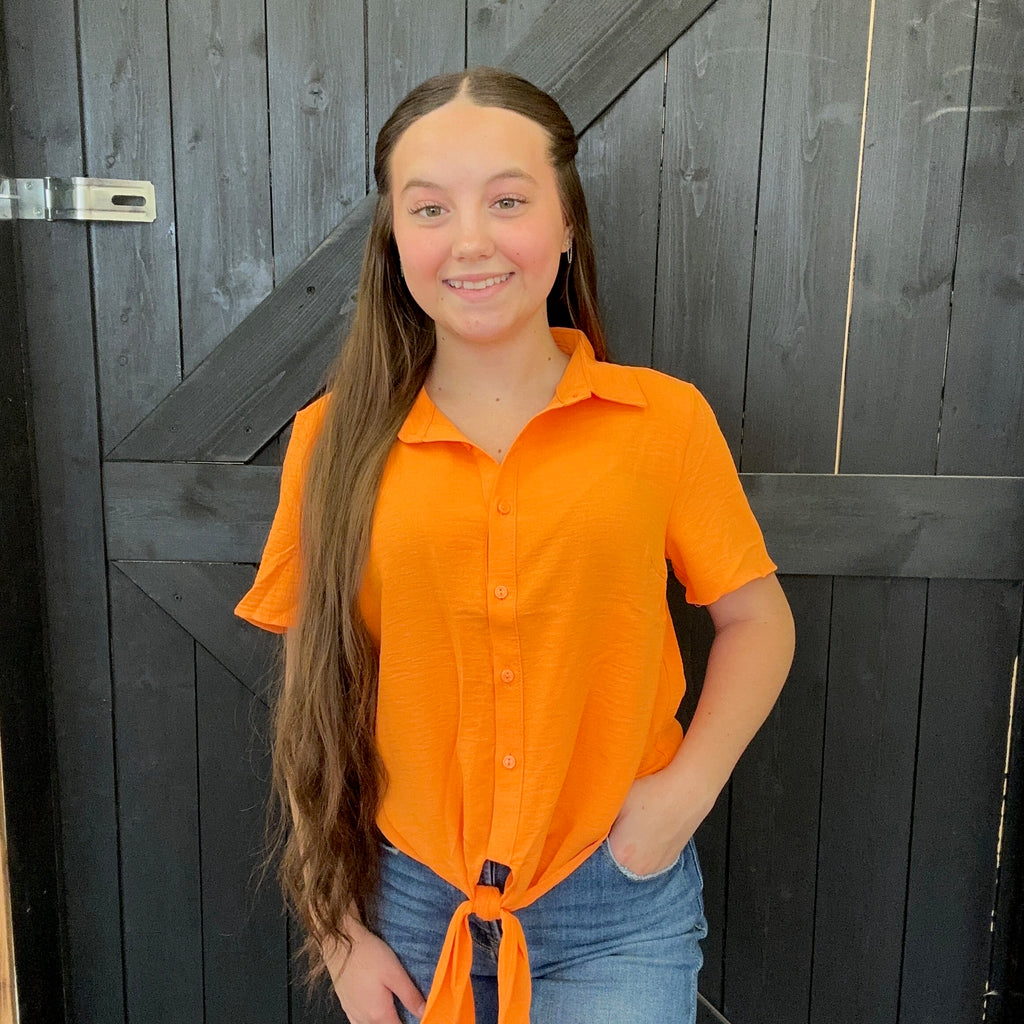Person wearing an orange shirt and blue jeans standing in front of a wooden door.