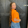 Person wearing an orange shirt and blue jeans standing against a wooden background