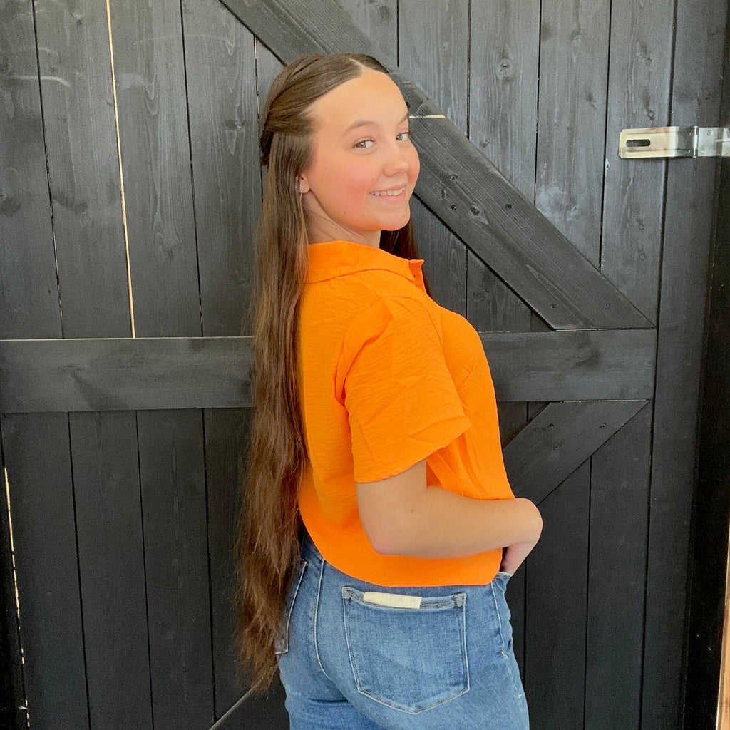 Person wearing an orange shirt and blue jeans standing against a wooden background