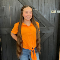 Person wearing an orange shirt and blue jeans standing against a wooden background