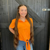 Person wearing an orange shirt and blue jeans standing against a wooden background