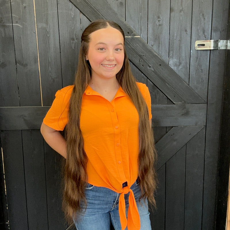 Person wearing an orange shirt and blue jeans standing against a wooden background