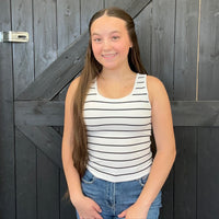 Young girl wearing a striped tank top and jeans standing in front of a wooden door.