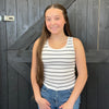 Young girl wearing a striped tank top and jeans standing in front of a wooden door.