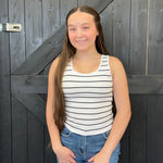 Young girl wearing a striped tank top and jeans standing in front of a wooden door.