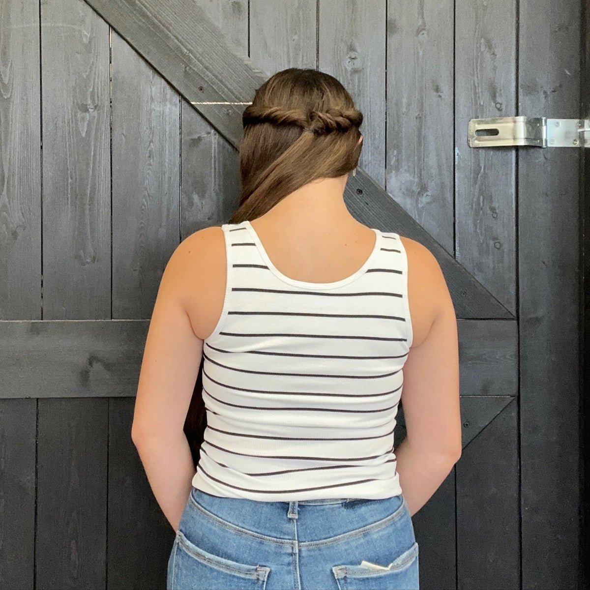 Person wearing a striped tank top and jeans standing in front of a wooden door.