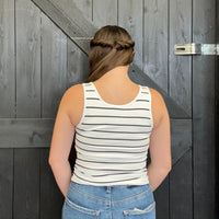 Person wearing a striped tank top and jeans standing in front of a wooden door.