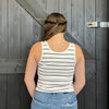 Person wearing a striped tank top and jeans standing in front of a wooden door.