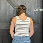 Person wearing a striped tank top and jeans standing in front of a wooden door.