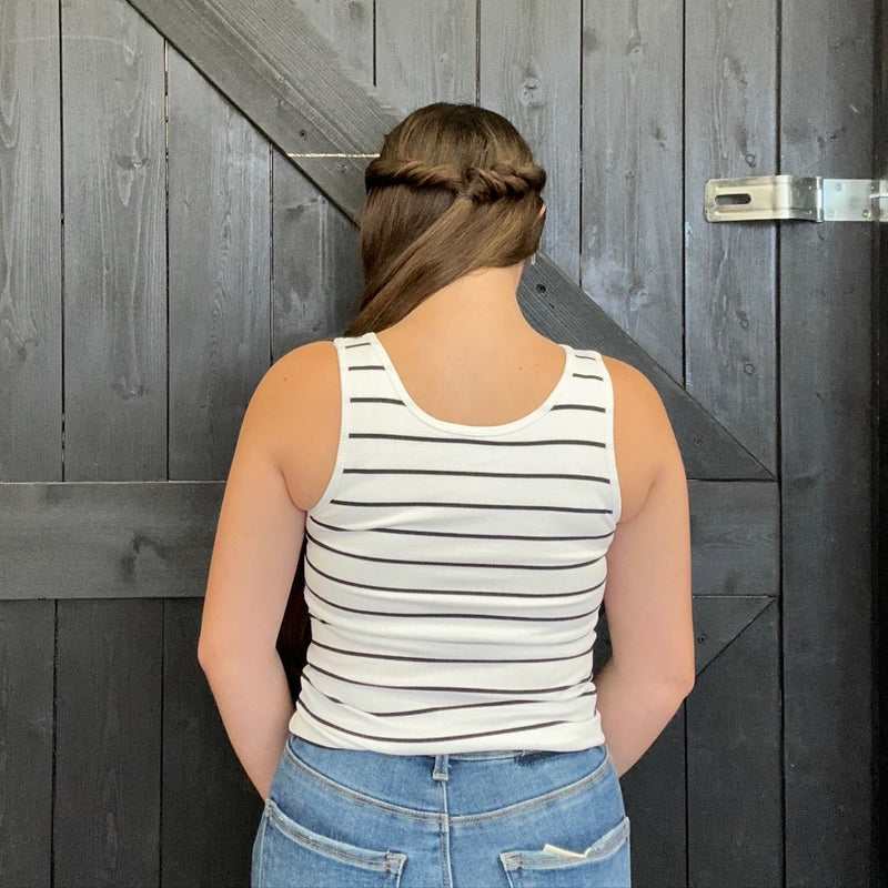 Person wearing a striped tank top and jeans standing in front of a wooden door.