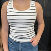 Person wearing a white tank top with black stripes and blue jeans against a dark background