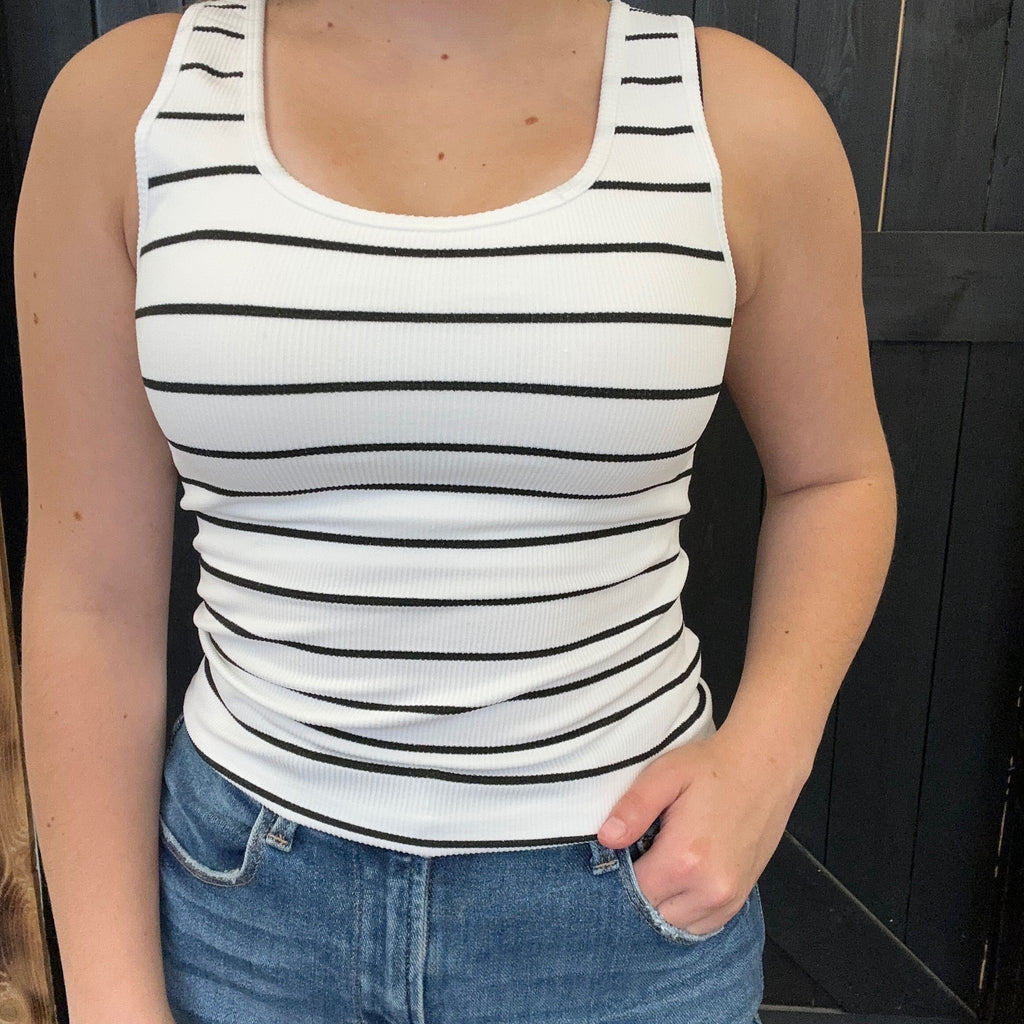 Person wearing a white tank top with black stripes and blue jeans against a dark background