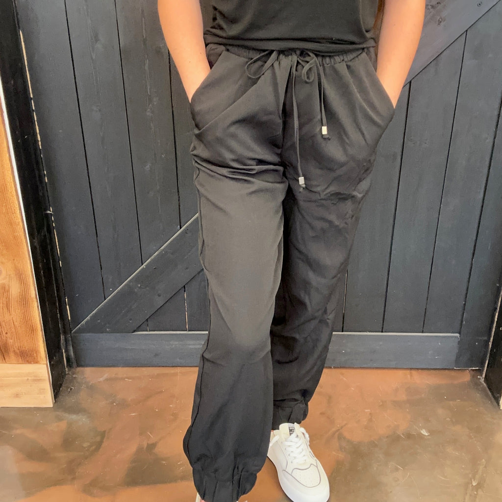 Person wearing black pants and white shoes standing against a wooden door.