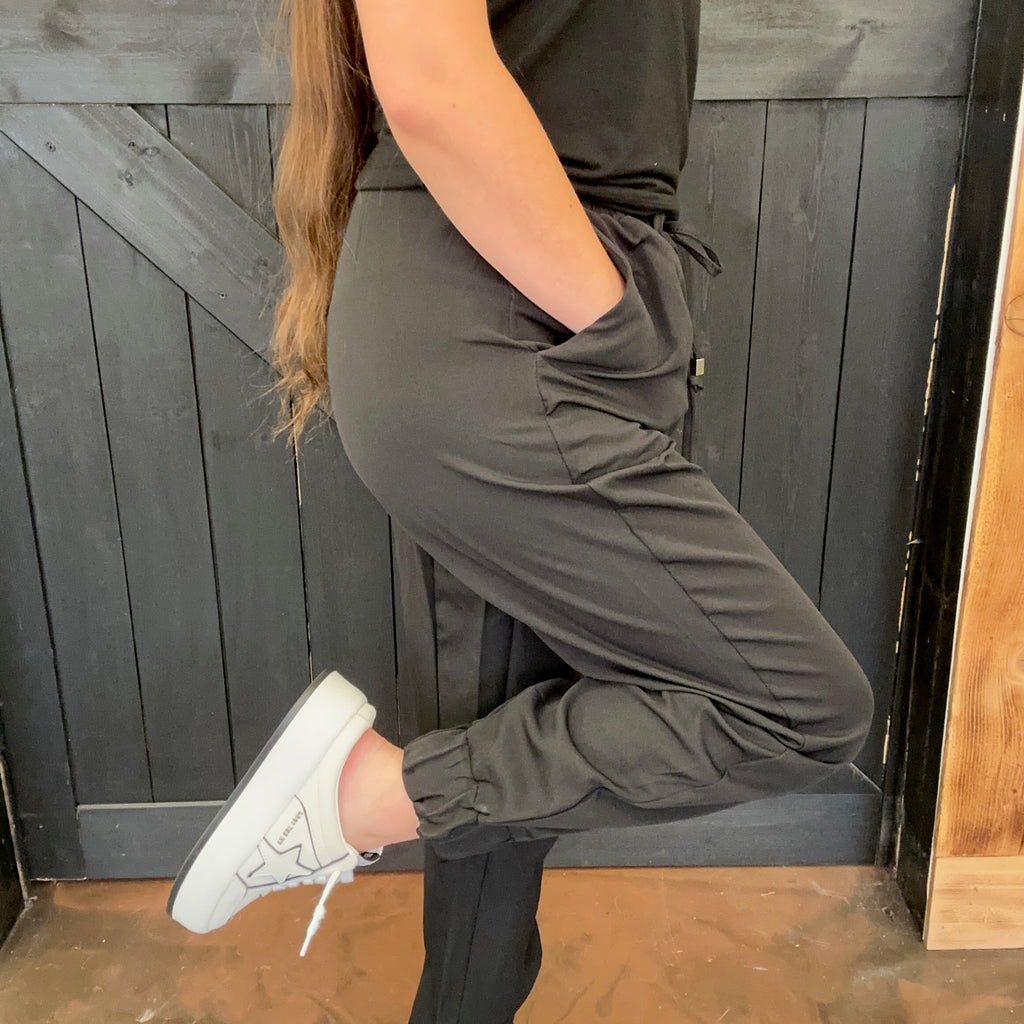 Person wearing a dark green outfit with white sneakers against a wooden background
