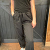 Person wearing a black outfit standing against a wooden wall.