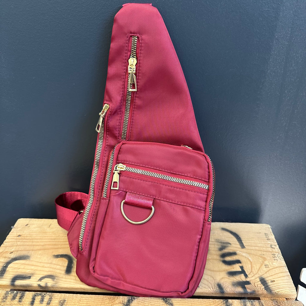 Pink sling bag with gold zippers on a wooden surface against a dark blue wall