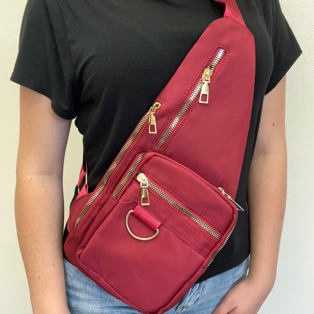 red sling bag with gold zippers on a plain background