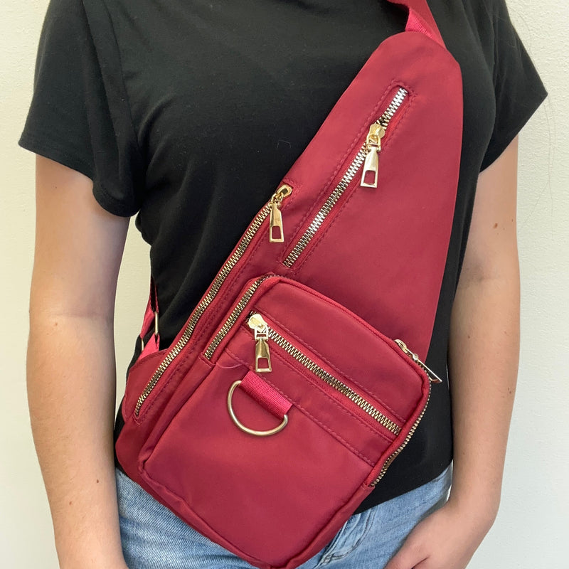 red sling bag with gold zippers on a plain background