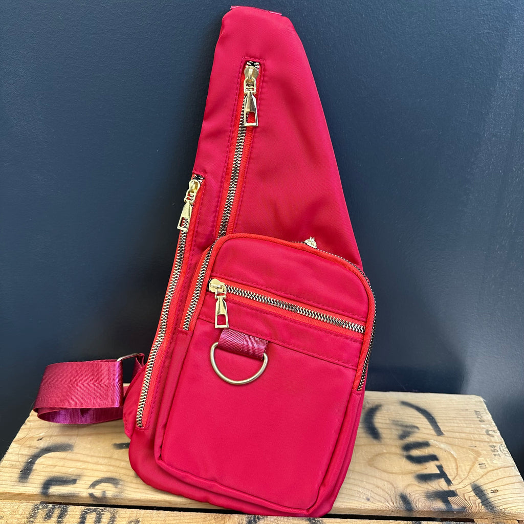 Red sling bag with gold zippers on a wooden surface against a dark blue background
