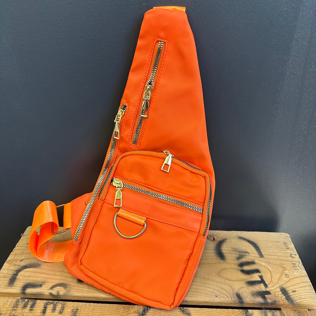 Orange sling bag with gold zippers on a wooden surface with graffiti.