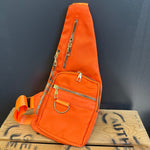 Orange sling bag with gold zippers on a wooden surface with graffiti.