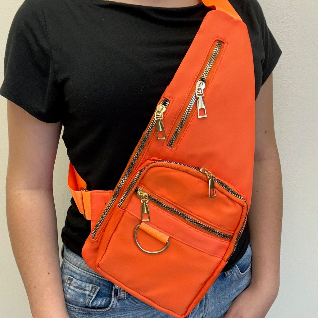 Person wearing an orange sling bag with gold zippers on a plain background