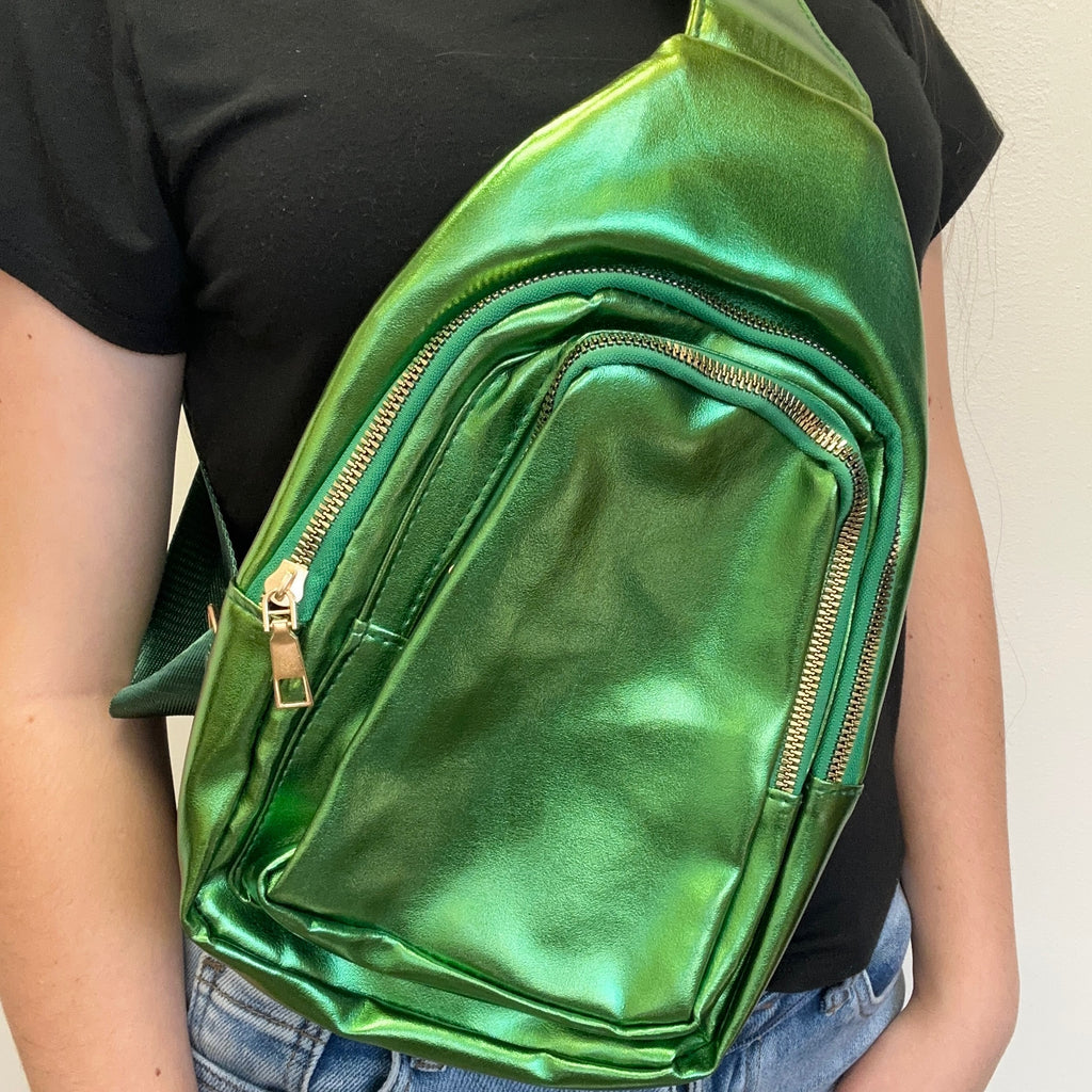 Green metallic sling bag worn by a person on a plain background