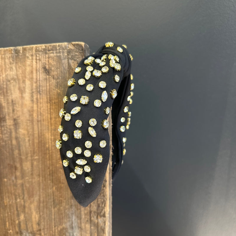 Black headband with gold and silver embellishments on a wooden block against a dark background