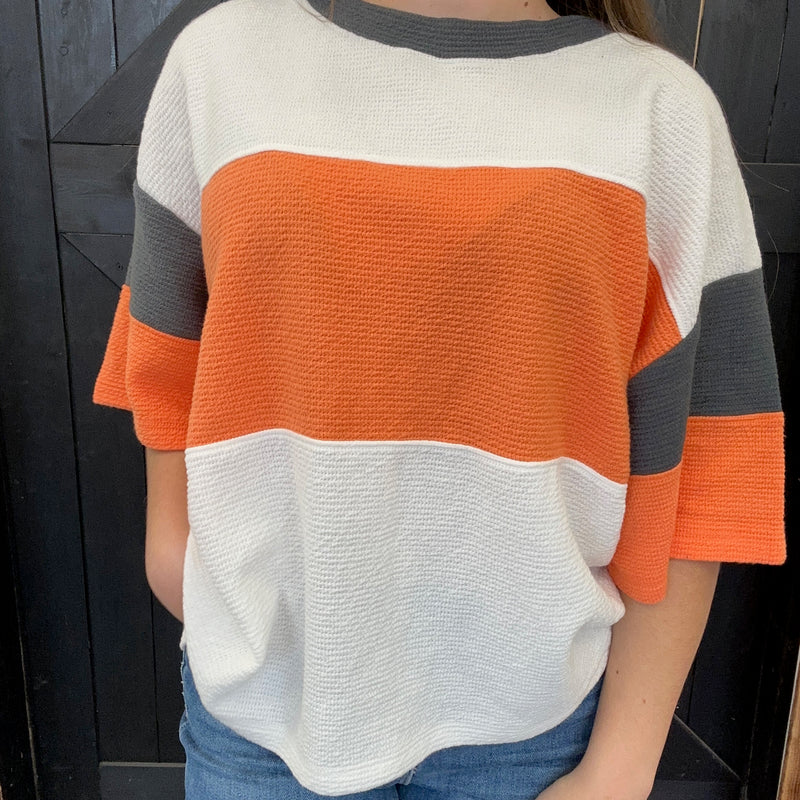 color-blocked sweater with orange, white, and gray sections.