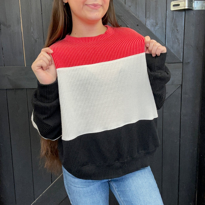 red, black, and white color-blocked sweater against a wooden background