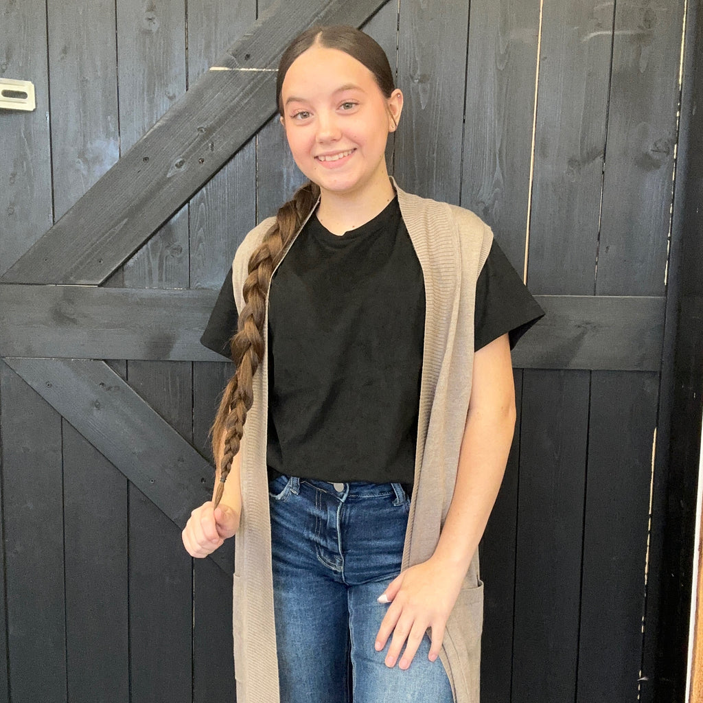  black shirt, beige cardigan, and blue jeans standing in front of a dark wooden door.
